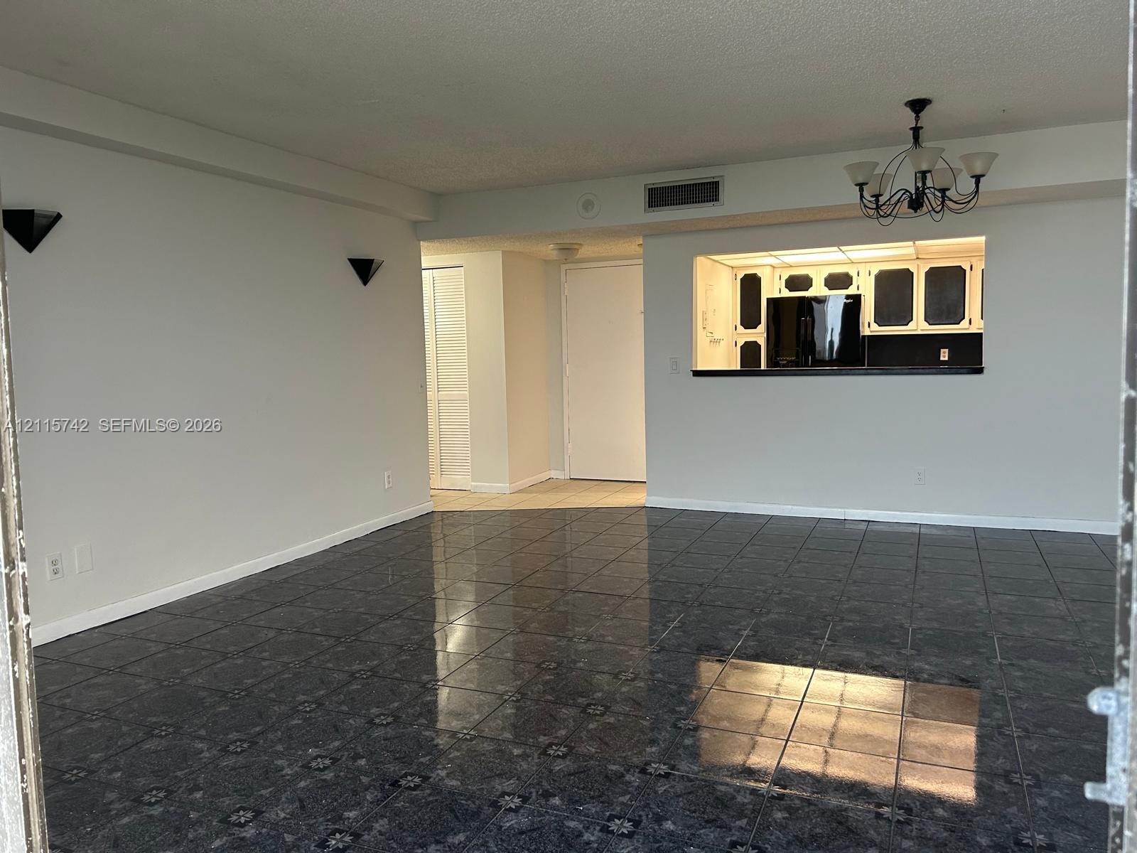 Glossy stone-look tile flooring, pass-through kitchen opening with breakfast bar, traditional multi-arm chandelier, and wall-mounted sconce lighting