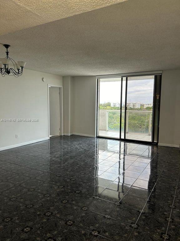 Living area featuring polished tile flooring, black metal chandelier, and floor-to-ceiling sliding glass doors leading to a balcony with glass railings