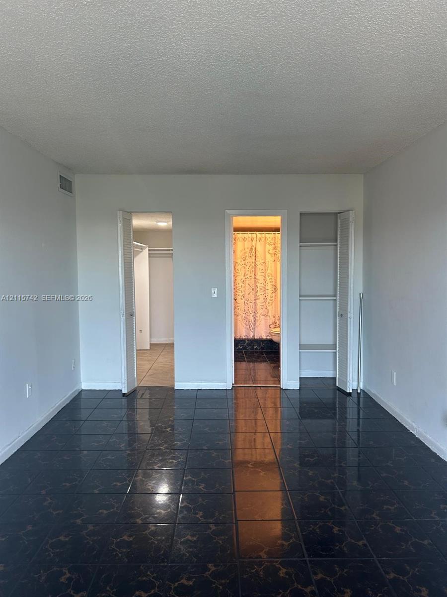 Dark-toned ceramic tile flooring, built-in shelving unit with louvered doors, walk-in closet with hanging rods, and an open doorway featuring a shower area