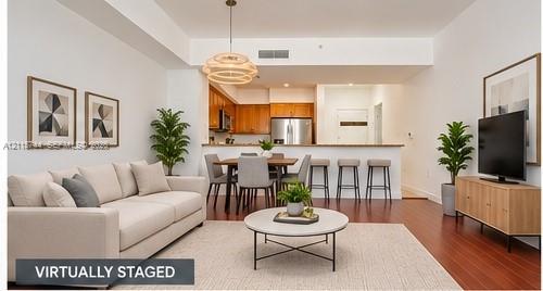 Open-concept floor plan featuring wood-finish flooring, a tiered kitchen breakfast bar, stainless steel appliances, and a modern tiered drum pendant light fixture