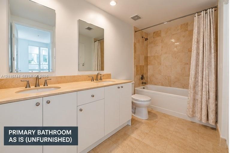 Dual-sink vanity with stone countertop, tile tub surround, recessed lighting, and tile flooring