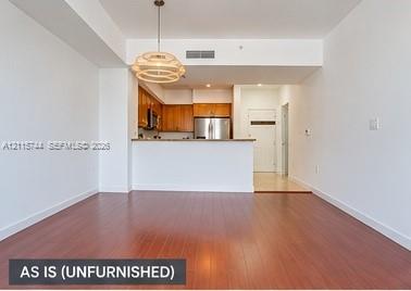 Open-concept area featuring wood-finish flooring, a kitchen breakfast bar, wood cabinetry, stainless steel appliances, and a modern pendant light fixture