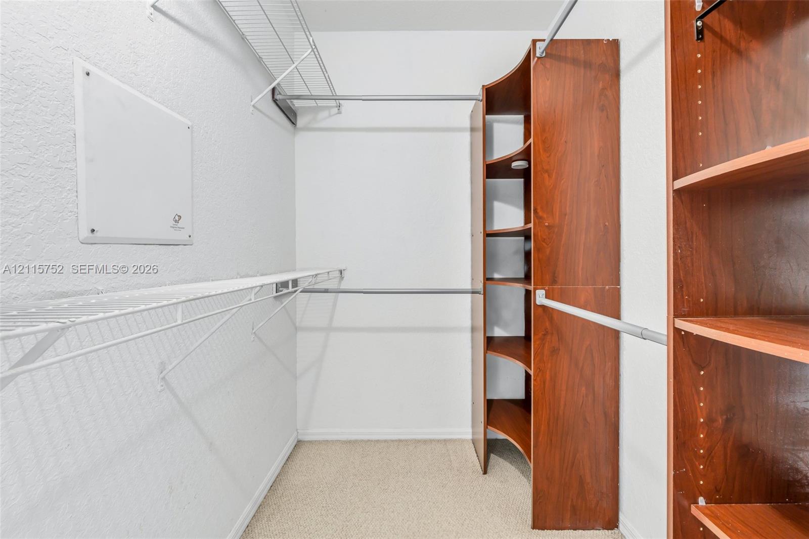 Walk-in closet featuring built-in wood-finish shelving, tiered metal wire racking, and neutral carpeting