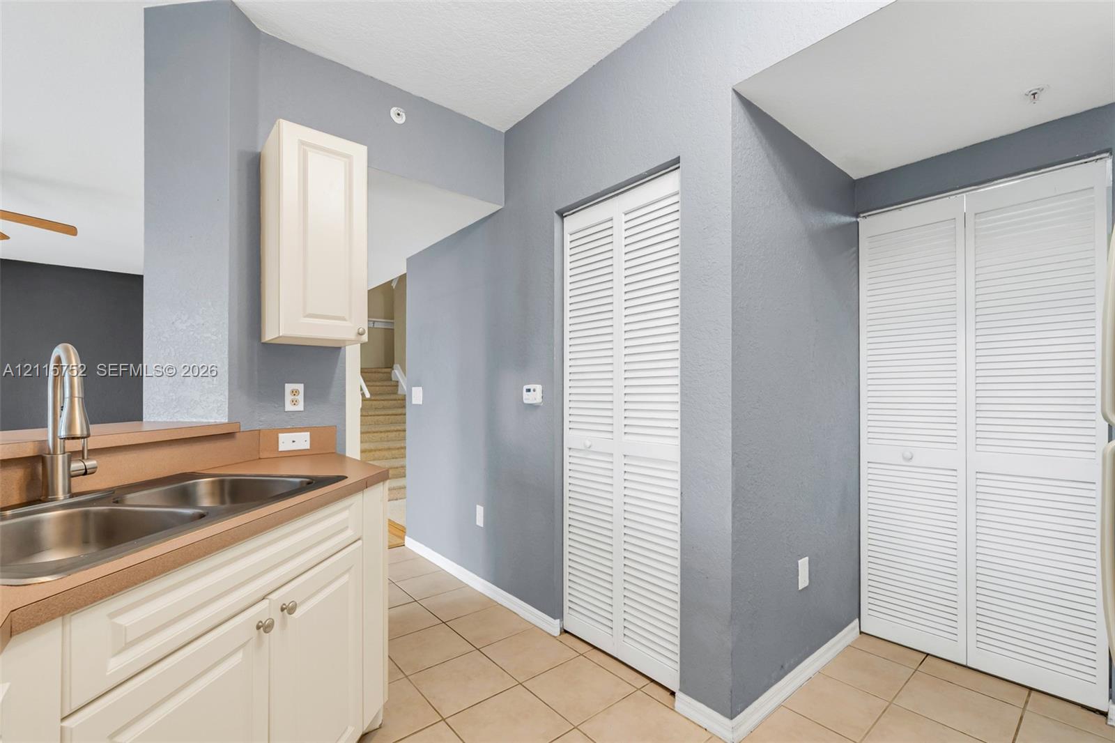 Kitchen featuring neutral tile flooring, white cabinetry with integrated hardware, dual-basin stainless steel sink, and louvered-door closets