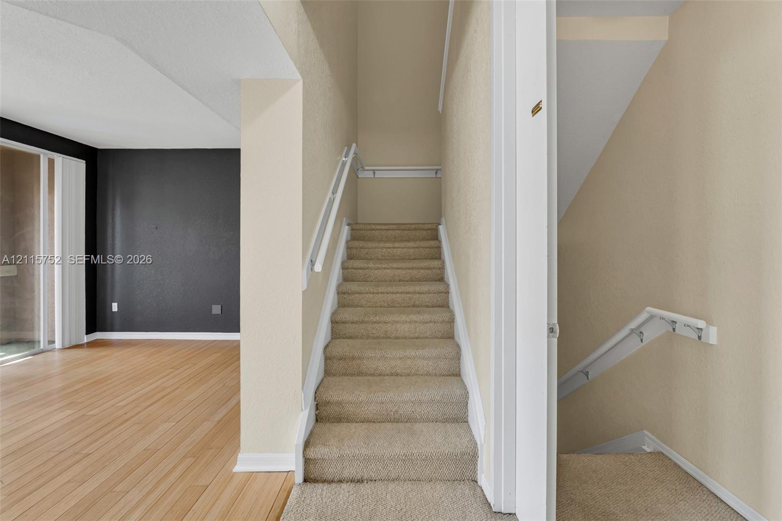 Staircase featuring wall-mounted railings and carpeted treads, wood-finish flooring, and a contrast wall