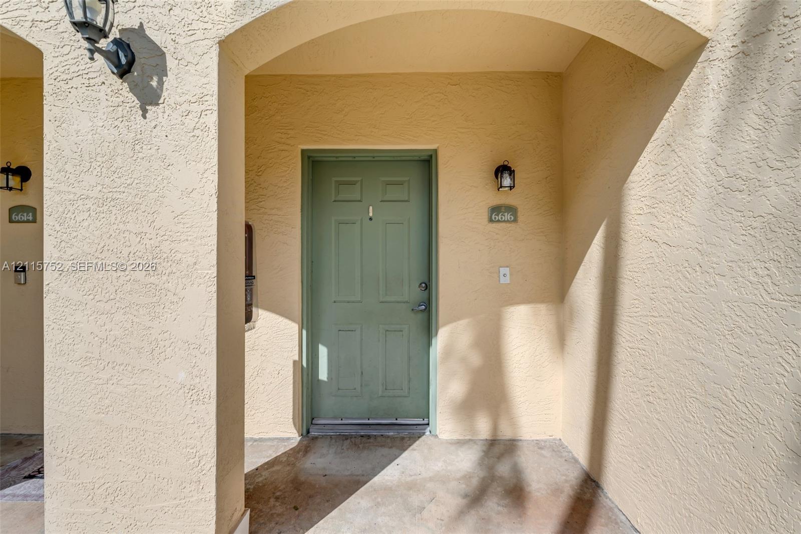 Stucco exterior entry featuring an arched recessed porch, six-panel entry door, and wall-mounted exterior lighting fixtures Stucco exterior entry featuring an arched recessed porch, six-panel entry door, and wall-mounted exterior lighting fixtures