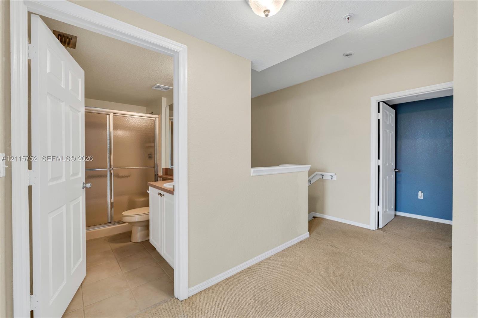 Upper-level landing featuring neutral carpeting, multi-panel interior doors, and a bathroom equipped with a glass-enclosed shower and white vanity cabinetry