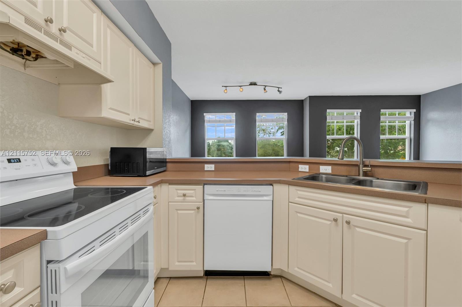 Kitchen featuring solid-color cabinetry, neutral-toned countertops, tile flooring, and a stainless steel double-basin sink