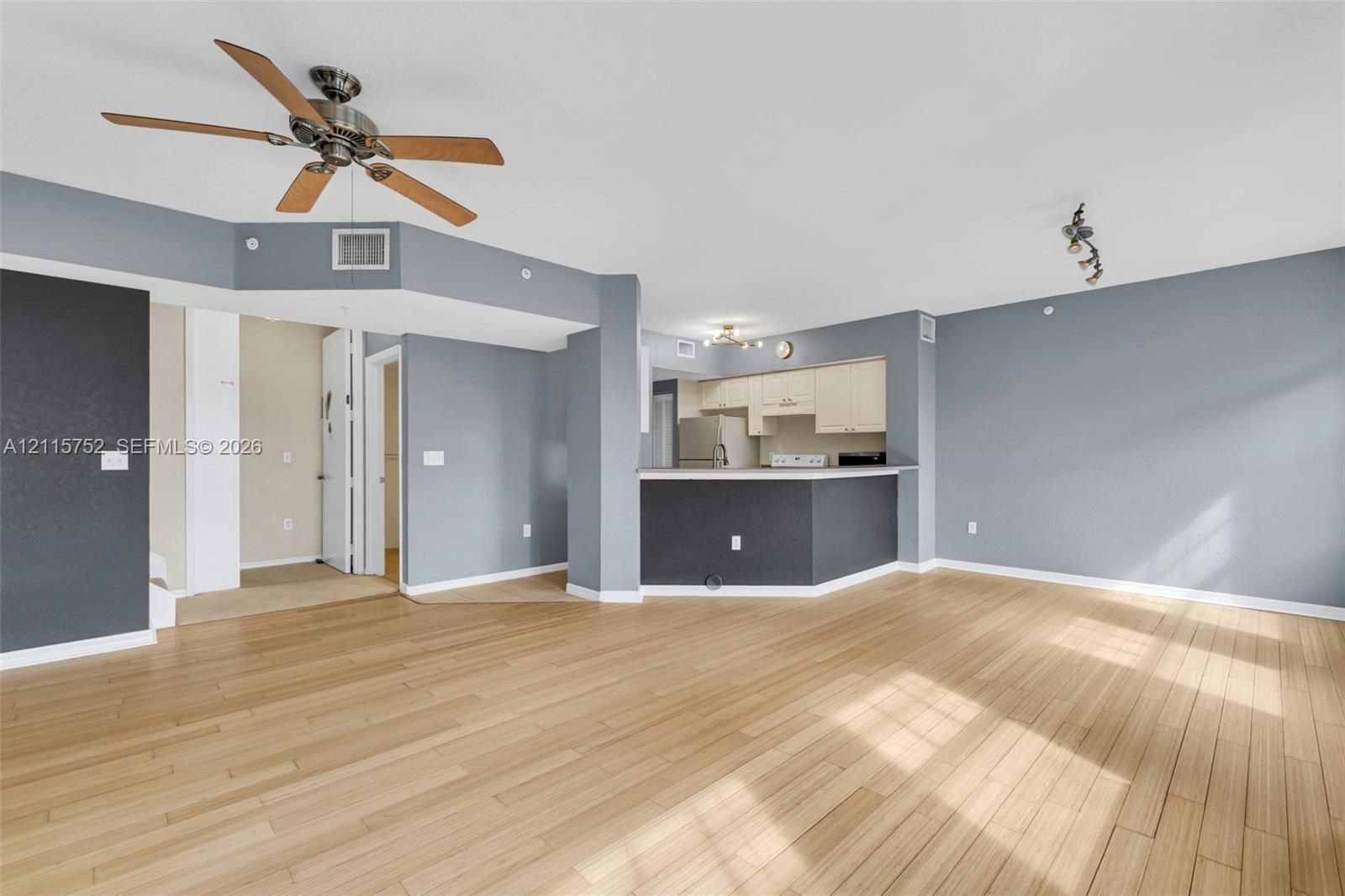 Wood-finish flooring, ceiling fan with wood-toned blades, breakfast bar with a solid surface countertop, and kitchen cabinetry
