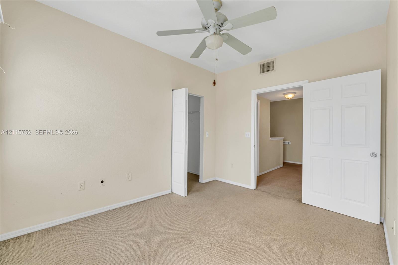 Neutral-toned room featuring carpeting, a white ceiling fan with integrated lighting, and a six-panel door