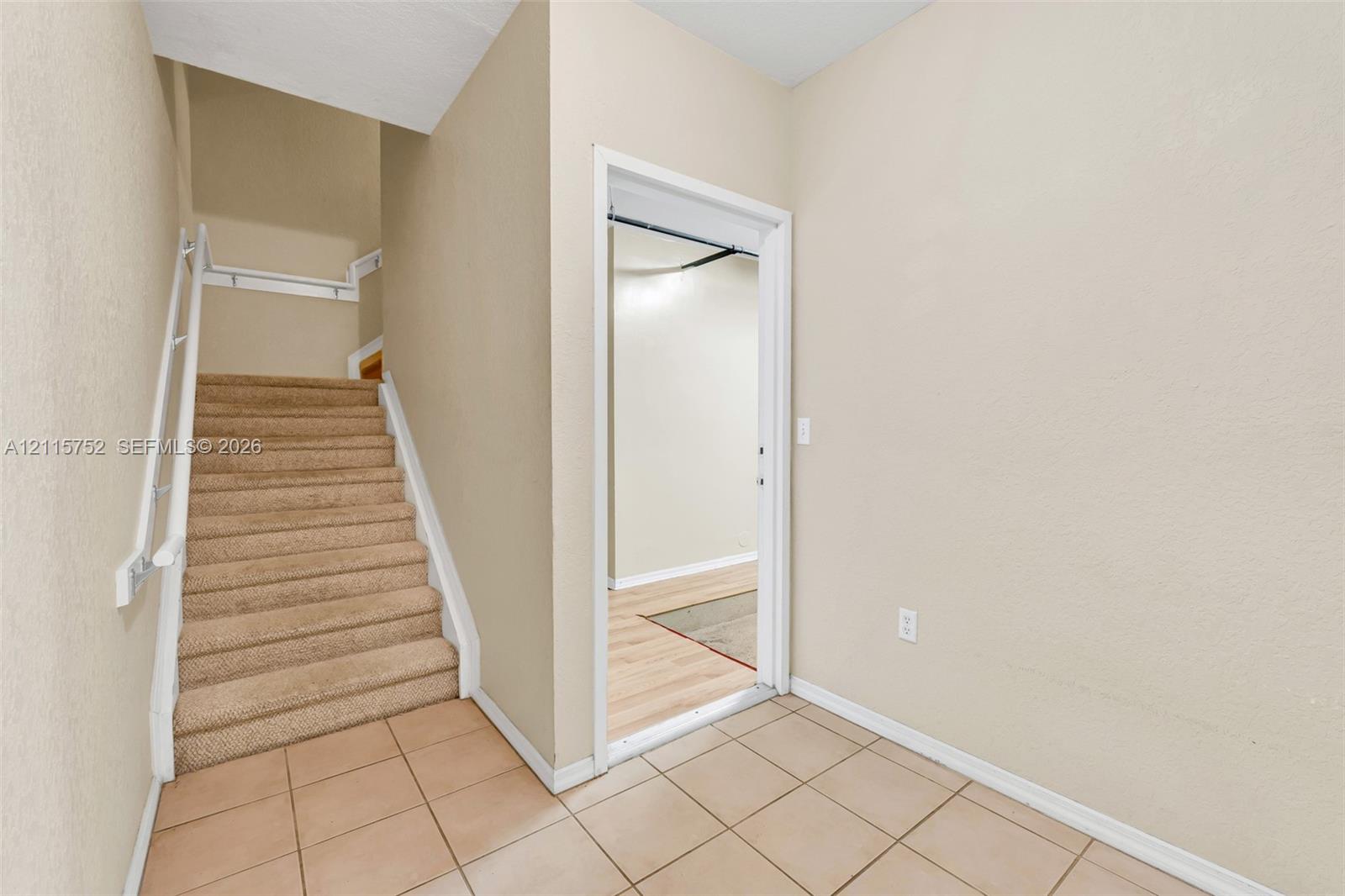 Interior entrance featuring neutral wall tones, carpeted staircase with white handrail, ceramic tile flooring, and interior door frame Interior entrance featuring neutral wall tones, carpeted staircase with white handrail, ceramic tile flooring, and interior door frame