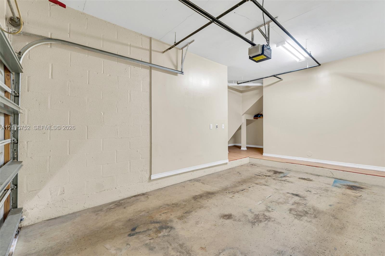 Enclosed garage featuring painted concrete block walls, overhead garage door hardware, ceiling-mounted light fixtures, and concrete flooring