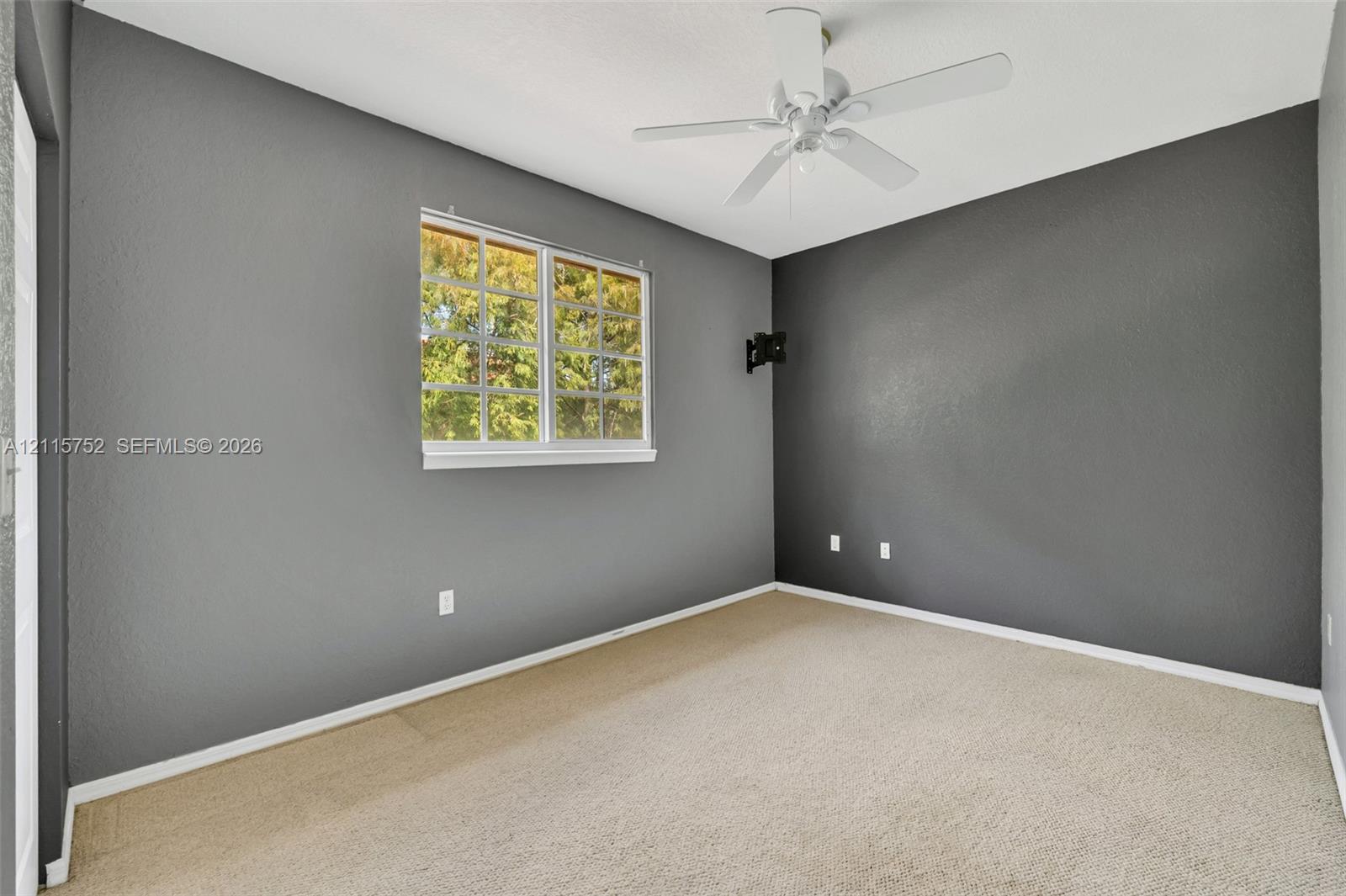 Room featuring charcoal accent walls, neutral wall-to-wall carpeting, a multi-pane window, and a ceiling fan with integrated lighting