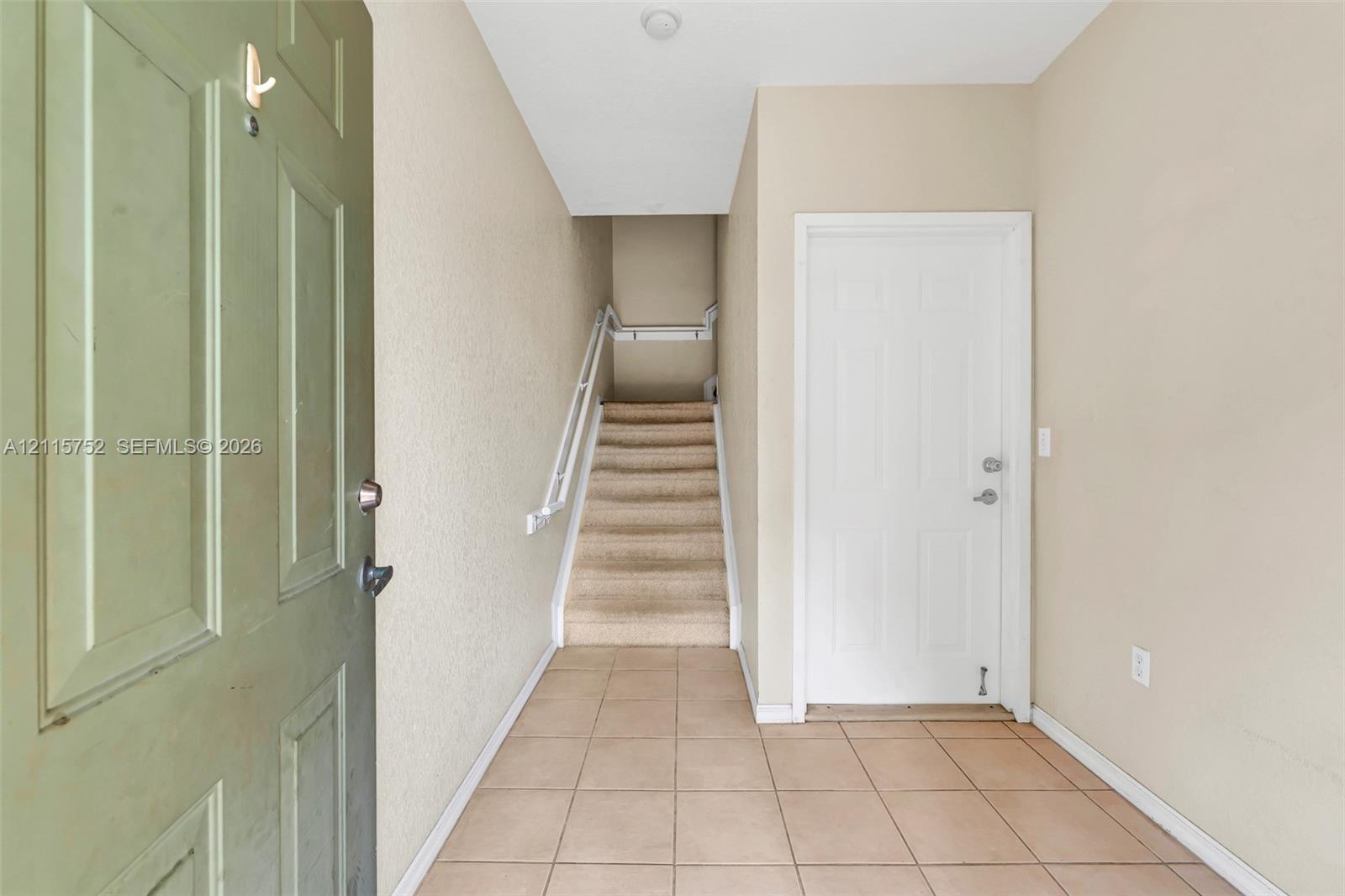 Entryway featuring ceramic tile flooring, a paneled door, and a carpeted staircase with a metal handrail Entryway featuring ceramic tile flooring, a paneled door, and a carpeted staircase with a metal handrail