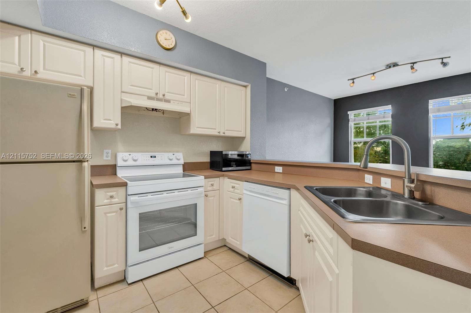 Kitchen featuring shaker-style cabinetry, solid-surface countertops, dual-basin stainless steel sink with pull-down faucet, tile flooring, and track lighting