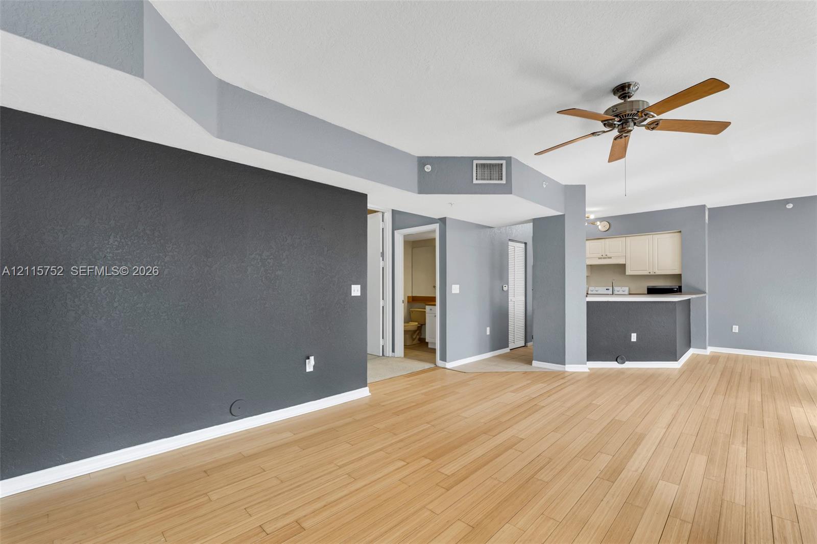 Interior featuring wood-finish flooring, accent wall, tray ceiling, ceiling fan, and kitchen breakfast bar