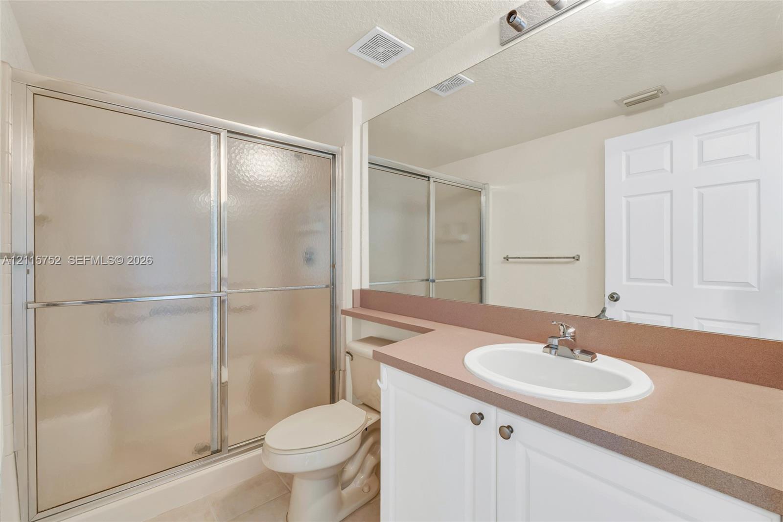 Bathroom featuring a white vanity with a solid-surface countertop, an integrated oval sink, a large wall-mounted mirror, and a walk-in shower with a sliding glass door