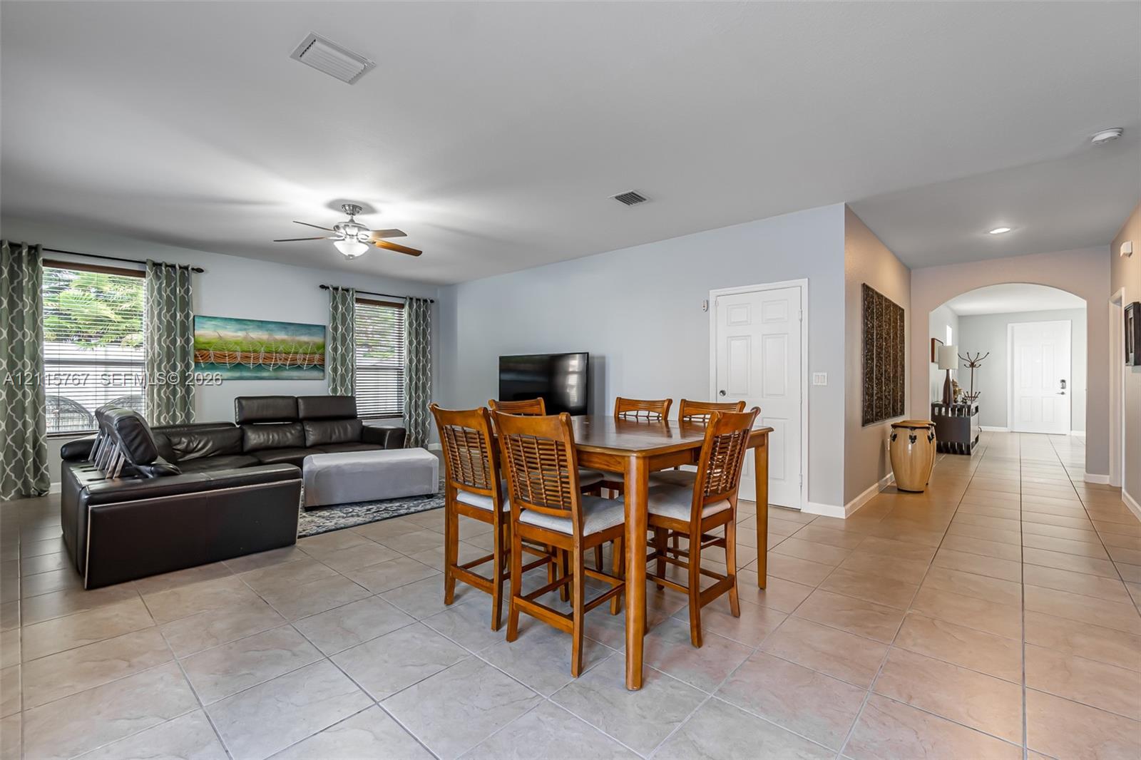 Open-concept interior featuring large-format ceramic tile flooring, neutral wall tones, arched entryway, and a central ceiling fan