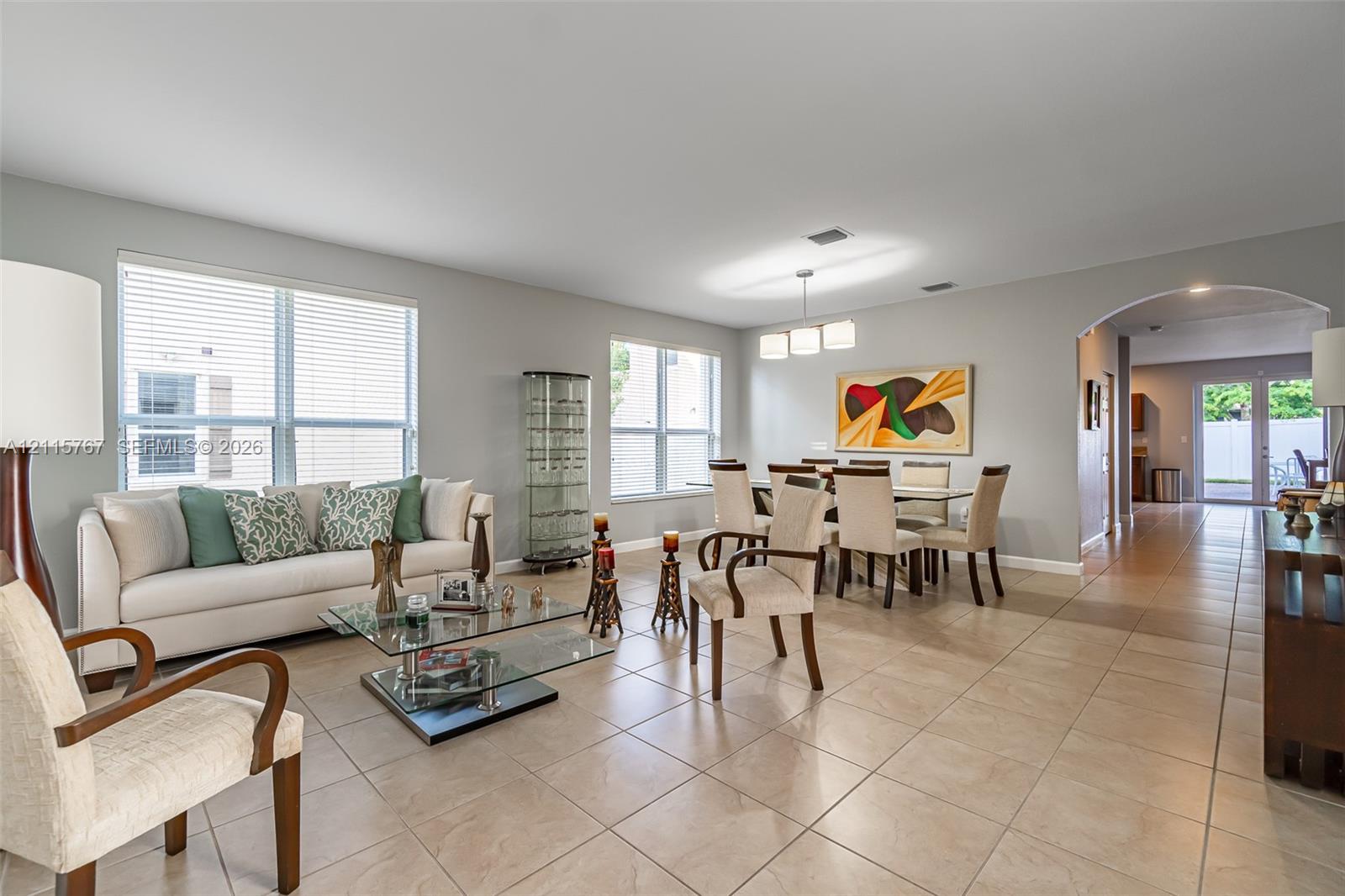 Open-concept space featuring large-format ceramic tile flooring, multiple windows providing natural light, a recessed arched entryway, and a built-in three-light modern chandelier
