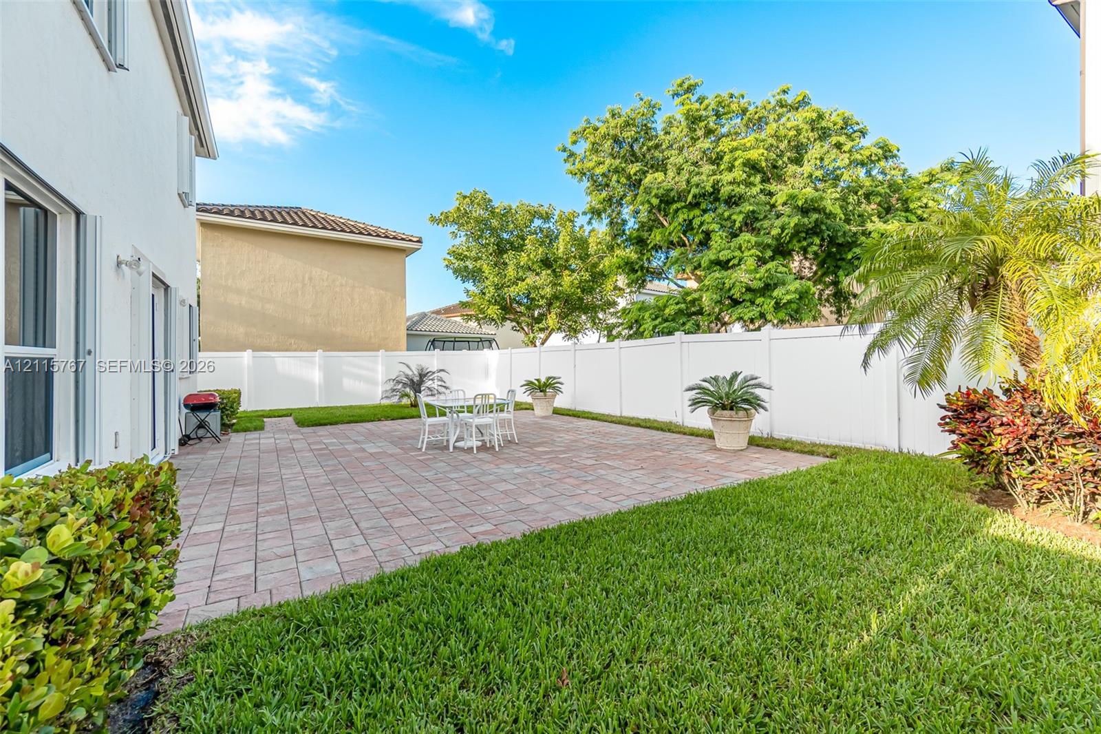 Private backyard featuring a paved patio, manicured lawn, perimeter vinyl fencing, and mature landscaping