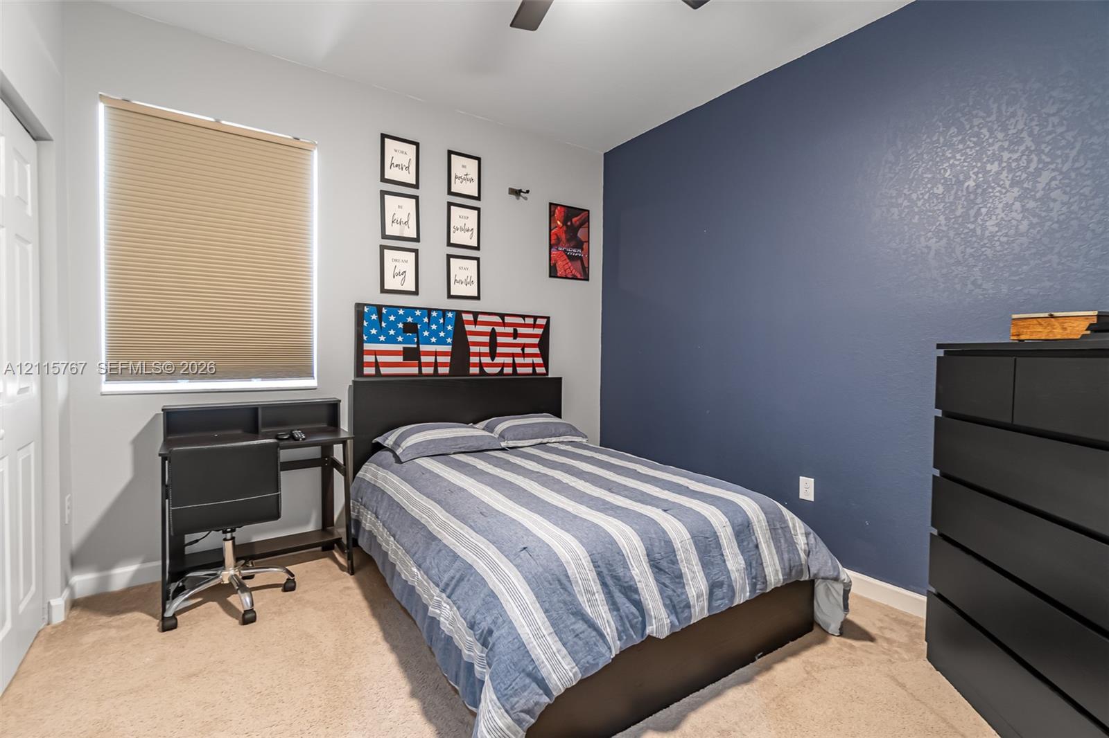 Neutral-toned carpeting, accent wall painted in navy blue, pleated window shade, and ceiling fan