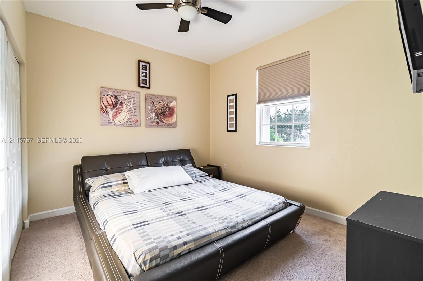 Neutral-toned interior featuring carpeting, a multi-pane window with a retractable shade, and a ceiling-mounted fan with an integrated light fixture