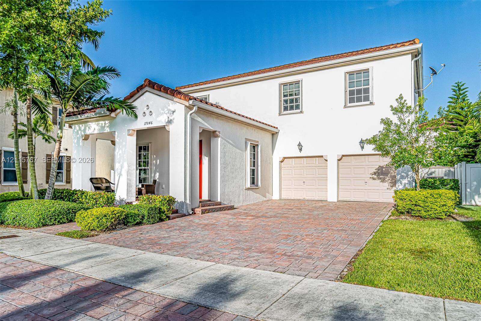 Stucco exterior with a tiled roof, covered entryway, and dual-car garage featuring paved driveway and mature landscaping Stucco exterior with a tiled roof, covered entryway, and dual-car garage featuring paved driveway and mature landscaping