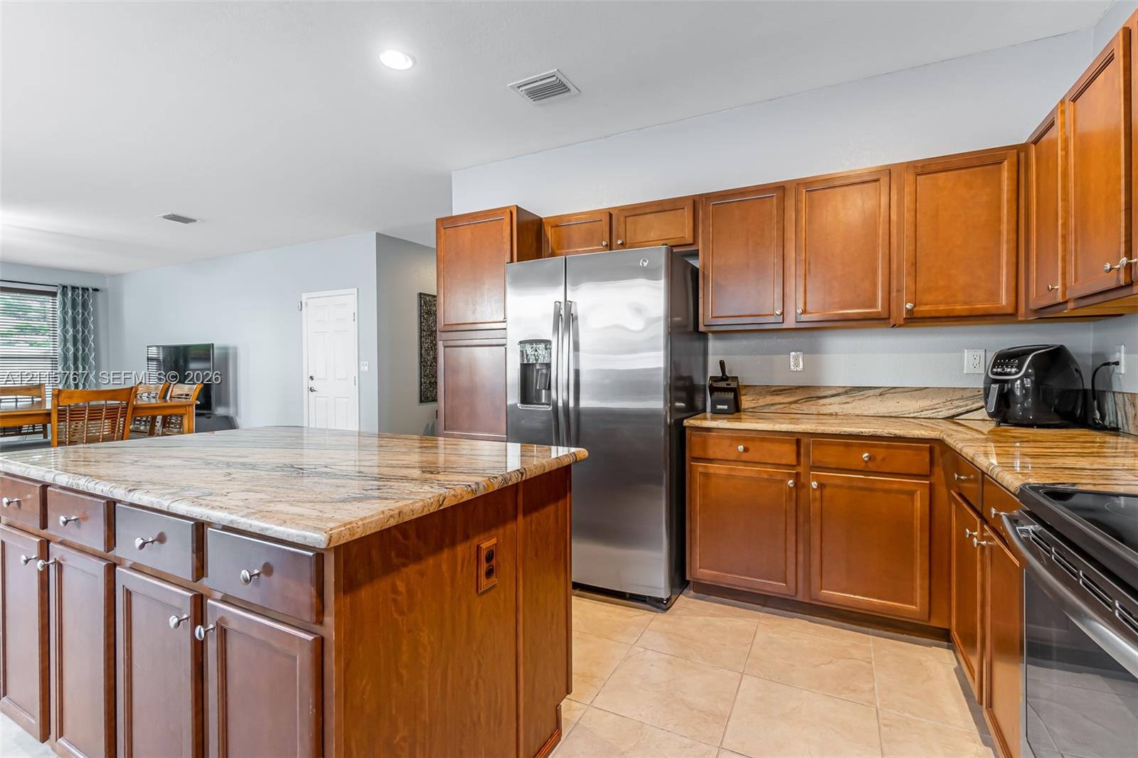 Kitchen featuring wood cabinetry, stone countertops, a center island, tile flooring, and stainless steel appliances