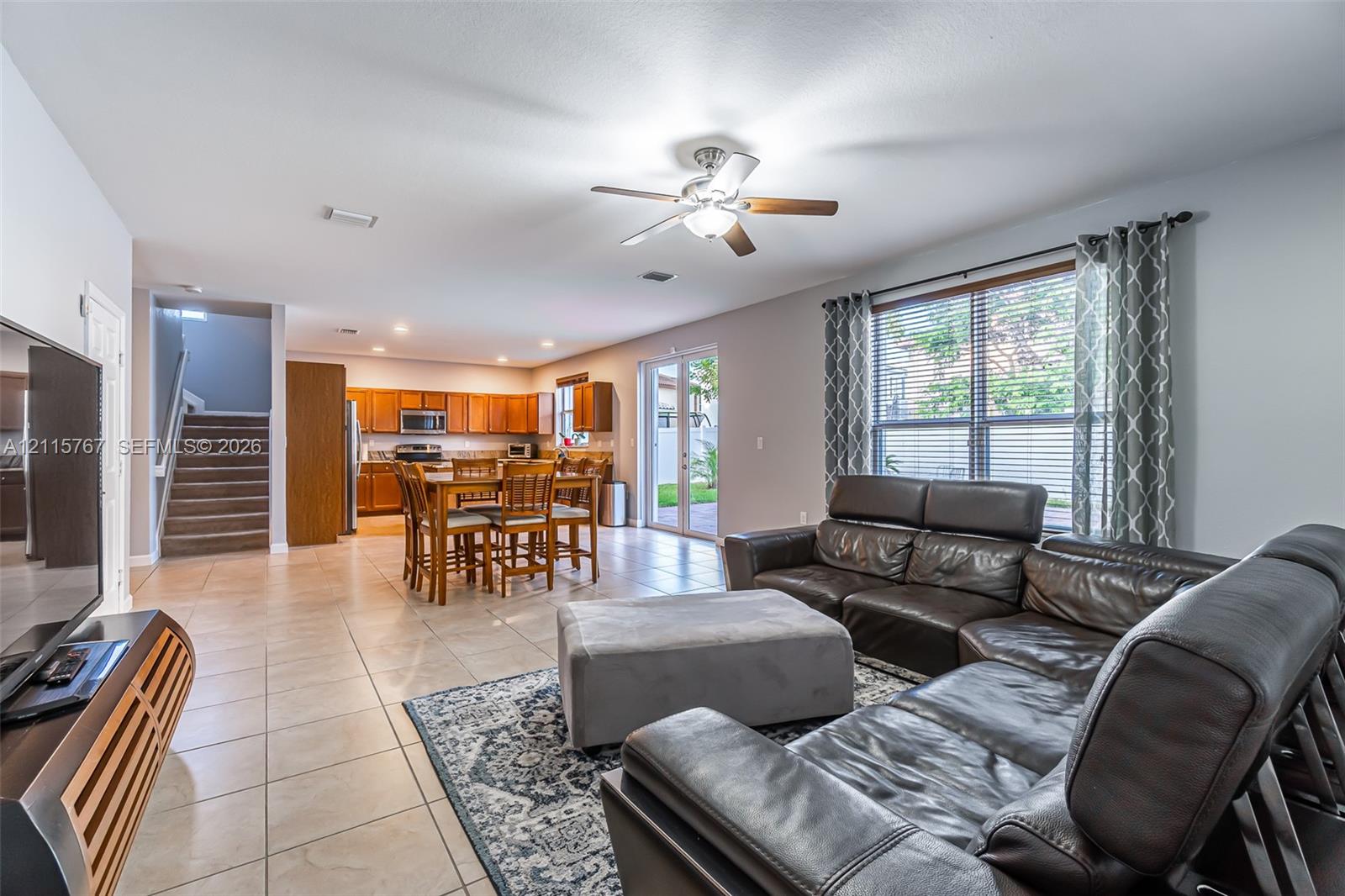 Open-concept floor plan featuring tile flooring, ceiling fan, wood-finish cabinetry, and glass sliding doors