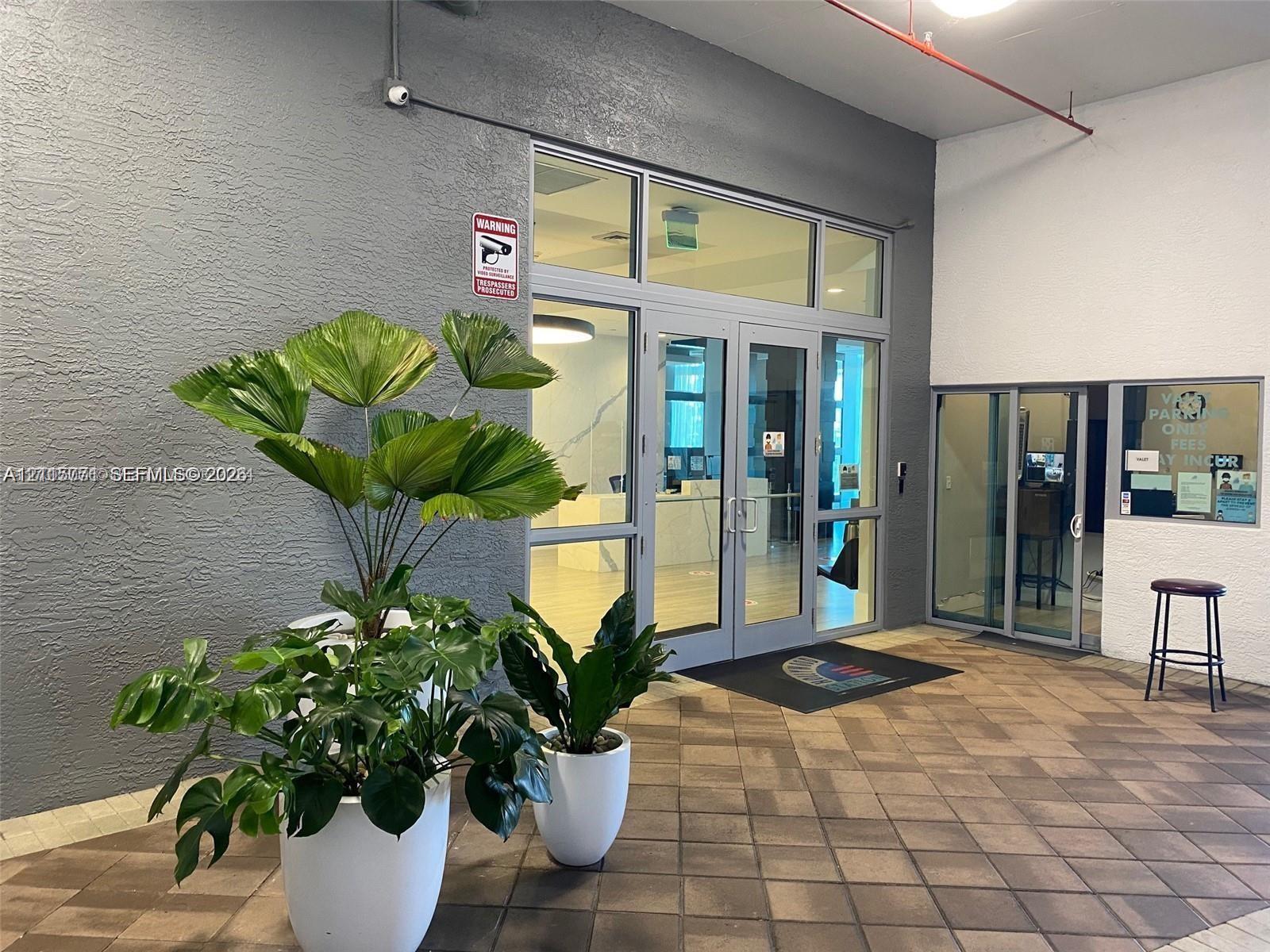 Entrance featuring glass-paneled double doors, textured gray exterior walls, and patterned paver flooring