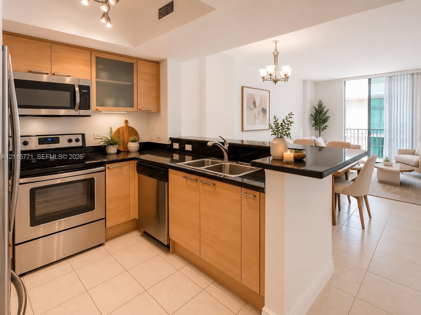Kitchen featuring light wood-finish cabinetry, black countertops, stainless steel appliances, a dual-basin sink, and tile flooring
