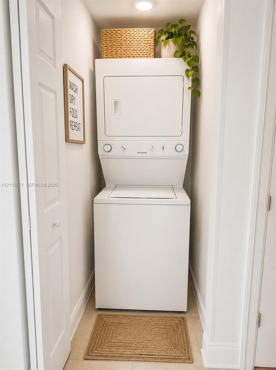 Stacked laundry unit with white finish, recessed ceiling lighting, and tile flooring