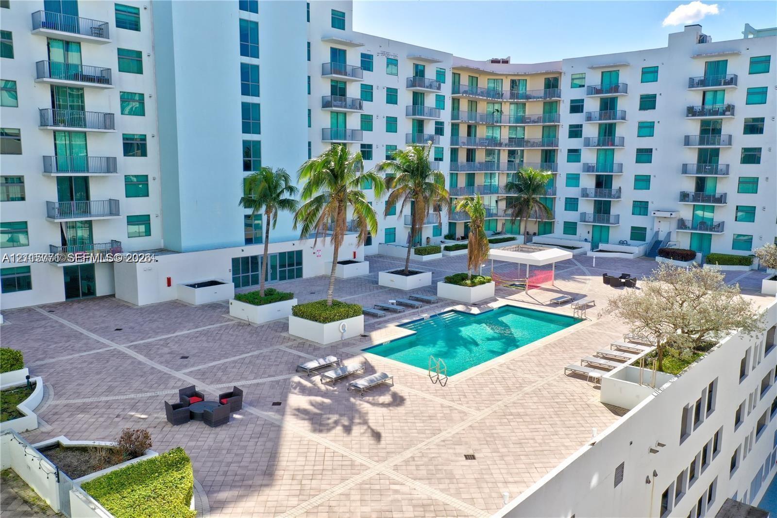 Outdoor courtyard featuring a swimming pool, paved sun deck, structured palm tree planters, and a shaded pergola