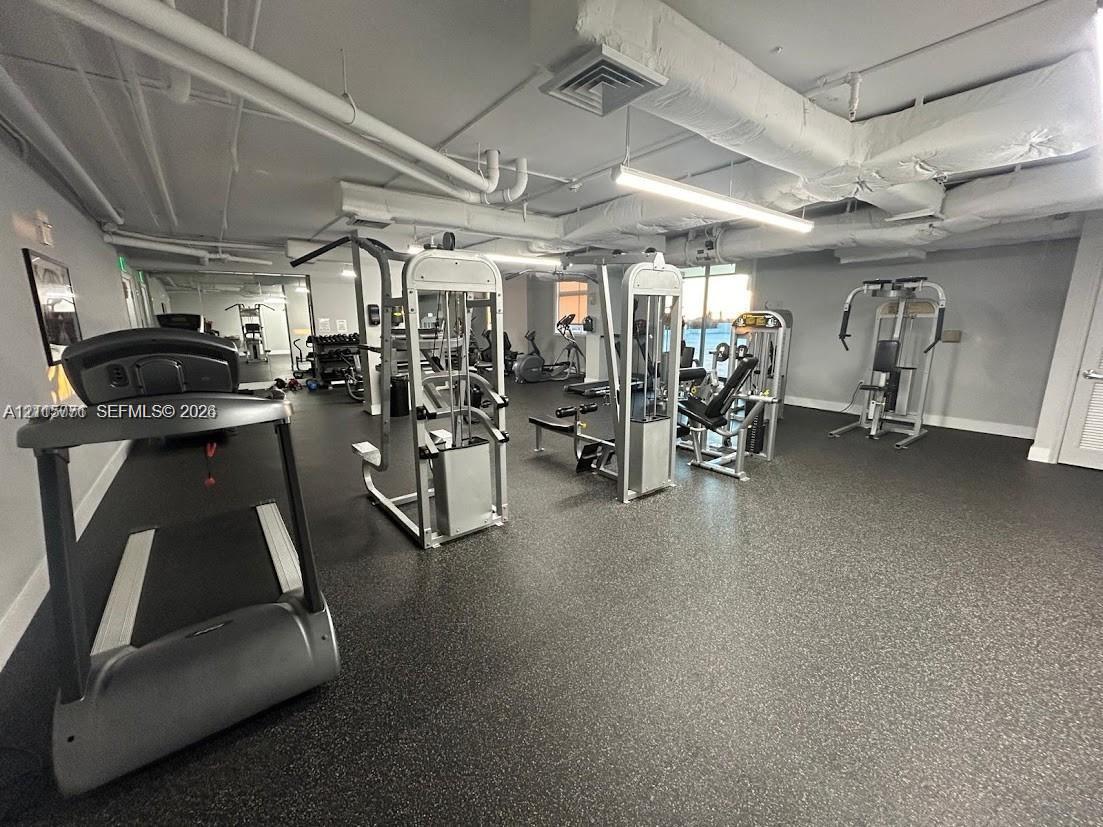 Fitness center featuring rubberized flooring, linear lighting, and an array of weight resistance and cardio equipment