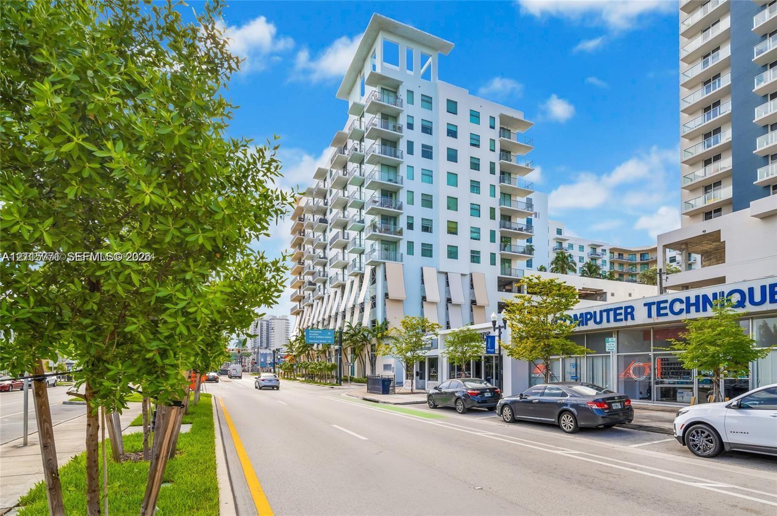 Multi-story concrete high-rise featuring tiered balconies, expansive glass window walls, and ground-level commercial space