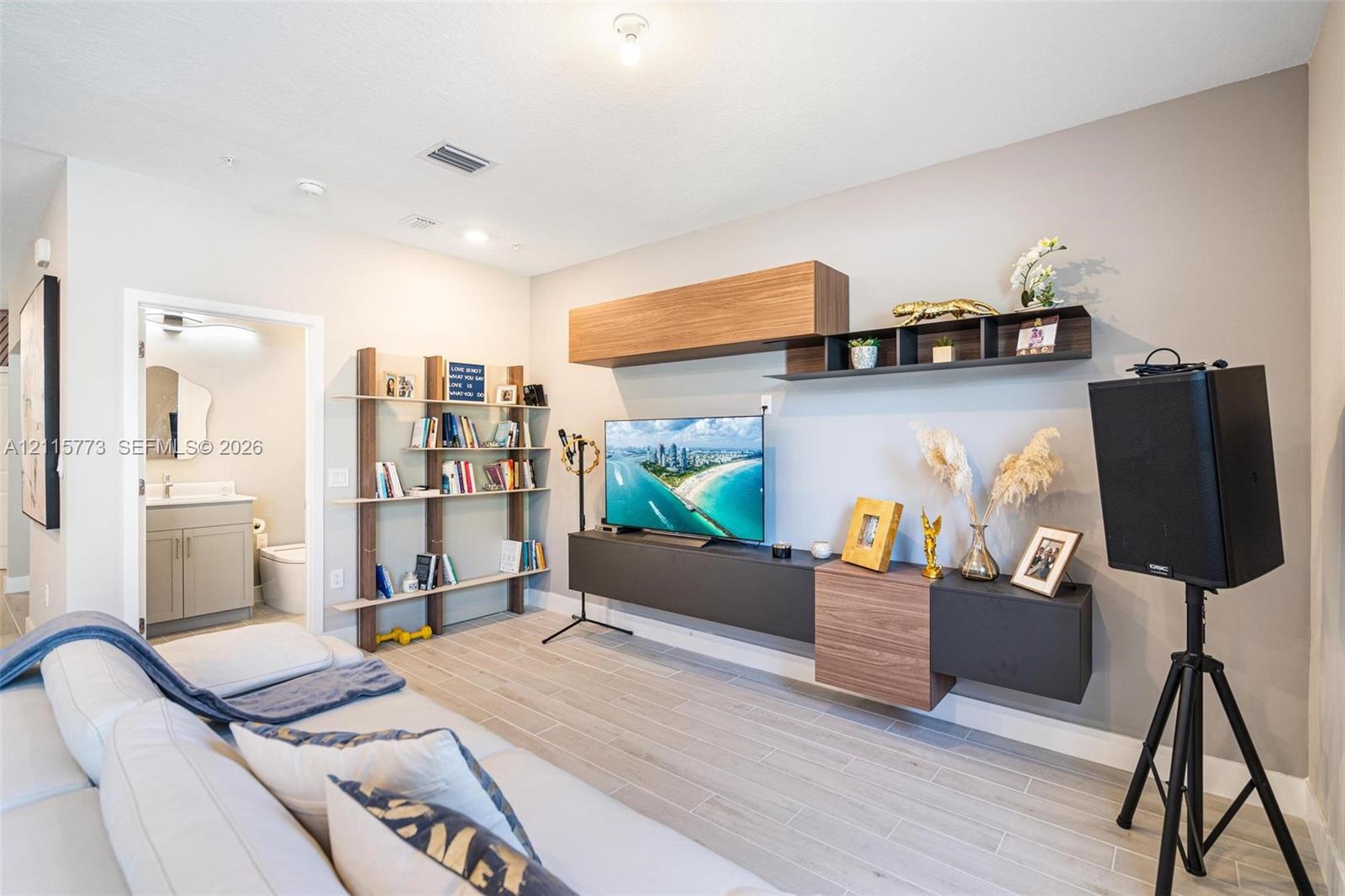 Living area featuring wood-finish flooring, a wall-mounted multi-piece media console with wood and matte-finish cabinetry, and a tiered built-in shelving unit