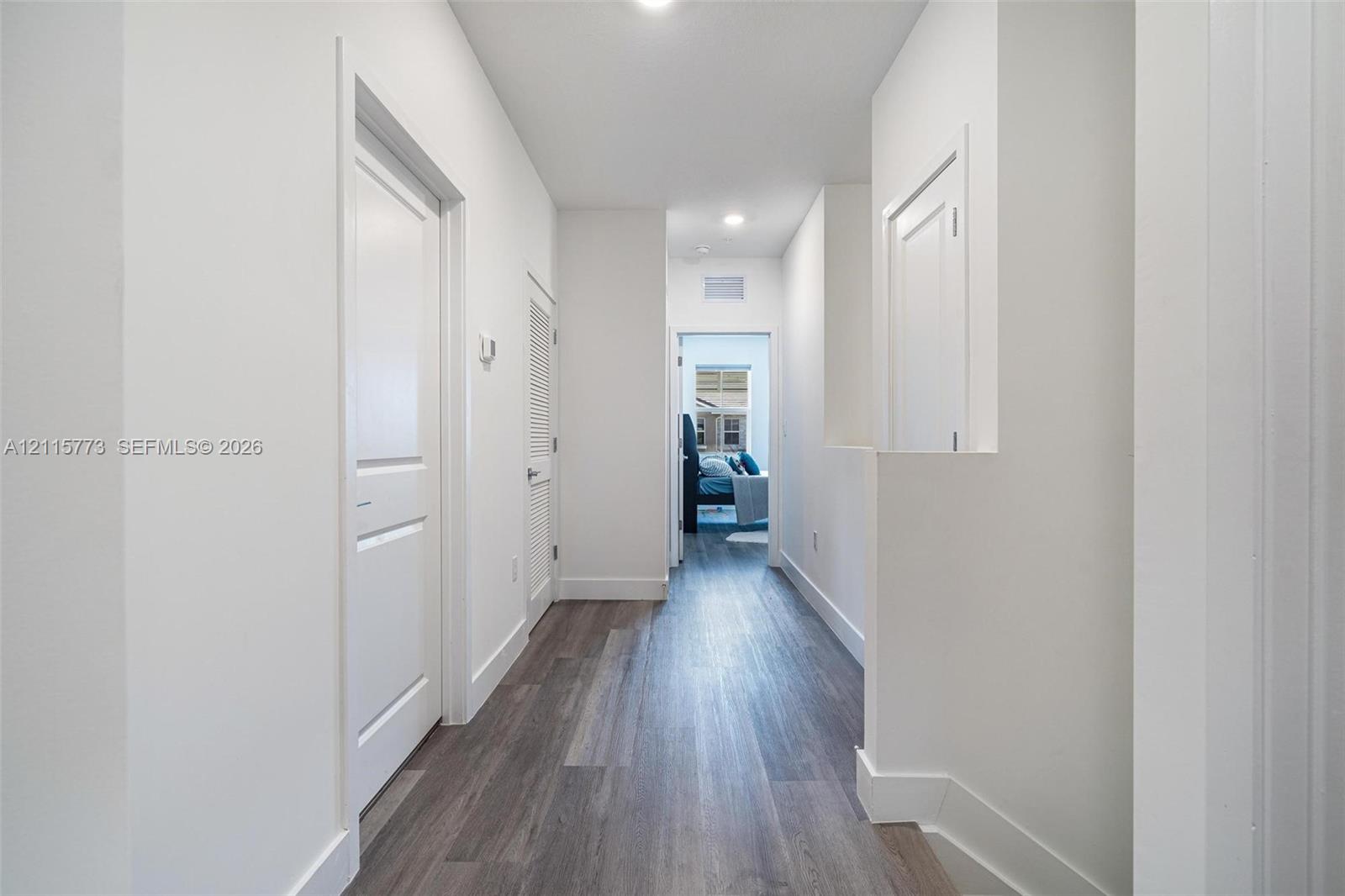 Hallway featuring wood-finish flooring, white paneled doors, recessed lighting, and crisp white wall finishes