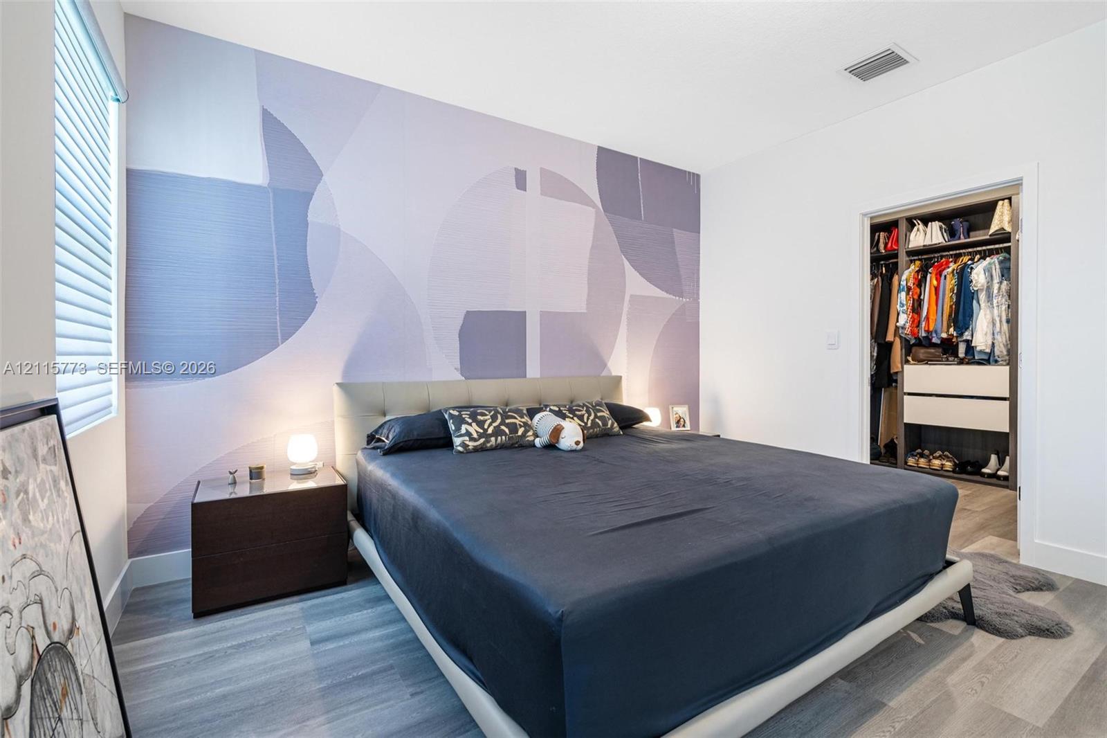 Room featuring a patterned accent wall, wood-finish flooring, and a walk-in closet with built-in shelving