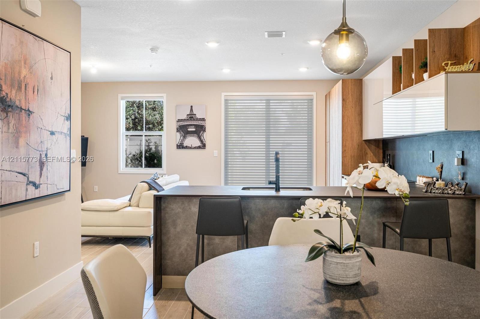 Kitchen featuring a central island with a sink and matte black faucet, gloss-finish upper cabinetry, open wood-tone shelving, and recessed lighting