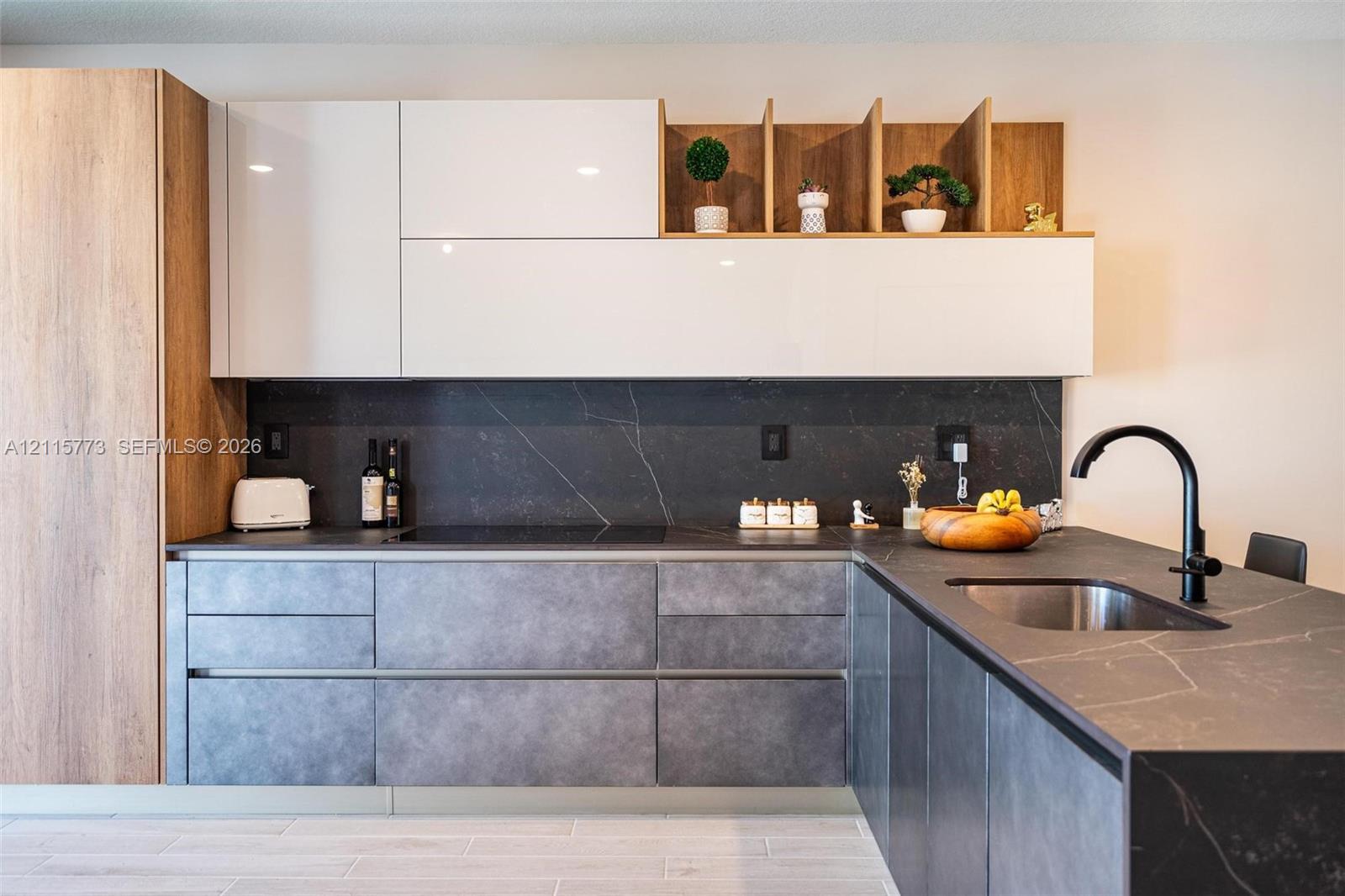 Modern kitchen featuring high-gloss white upper cabinetry, wood-finish accent shelving, textured matte lower cabinetry, dark stone-finish countertops with integrated backsplash, and a matte black gooseneck faucet Modern kitchen featuring high-gloss white upper cabinetry, wood-finish accent shelving, textured matte lower cabinetry, dark stone-finish countertops with integrated backsplash, and a matte black gooseneck faucet