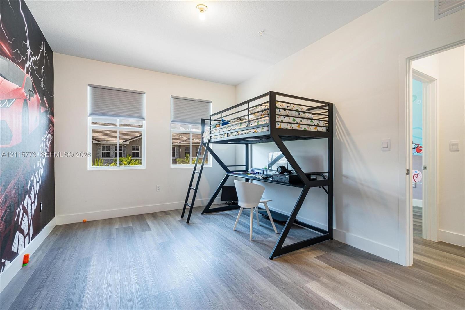 Spacious room featuring wood-finish flooring, dual windows with roller shades, and neutral wall paint