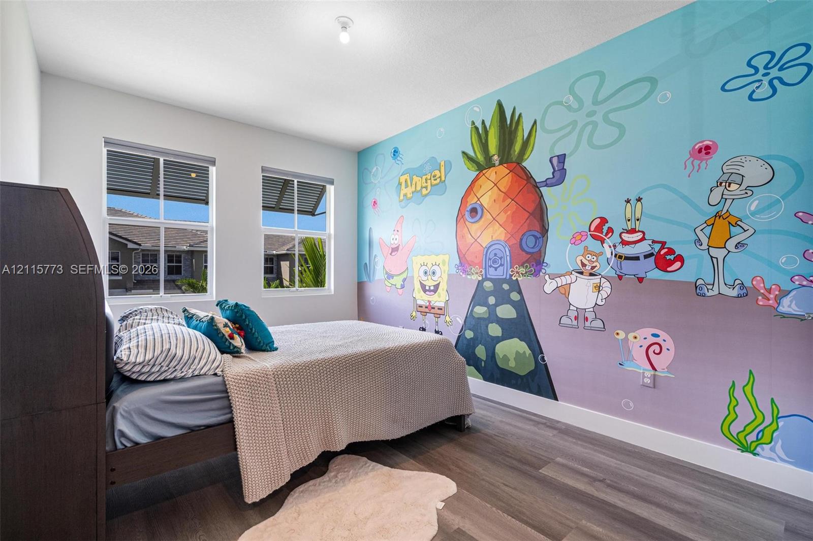 Bedroom featuring wood-finish flooring, dual windows with integrated blinds, and a full-wall custom mural