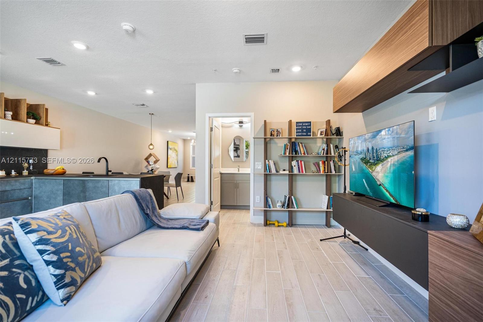 Open-concept interior featuring light wood-finish flooring, recessed lighting, and wall-mounted cabinetry with integrated shelving