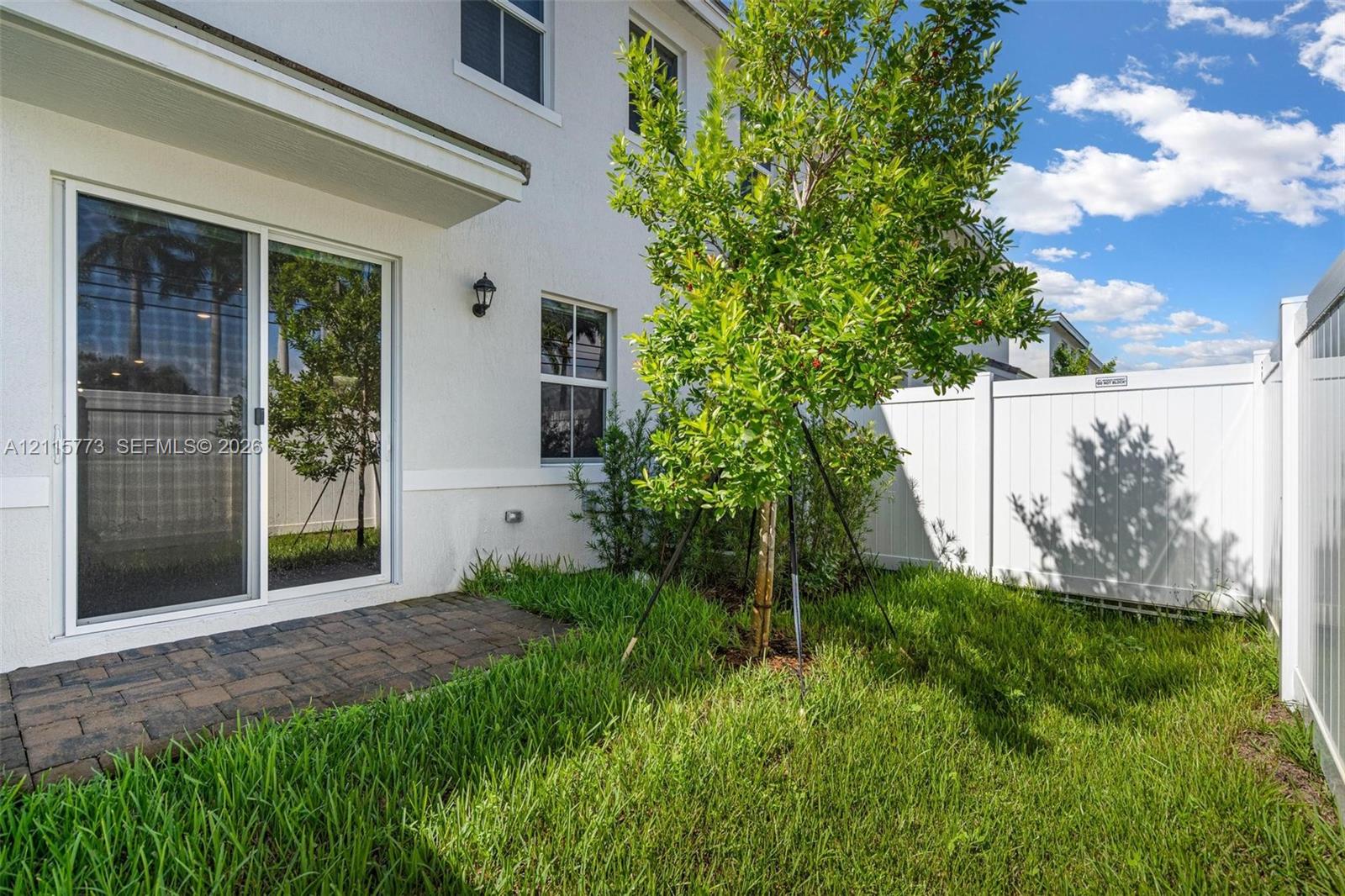 Paver patio, grass yard, white vinyl privacy fencing, and exterior wall-mounted lighting