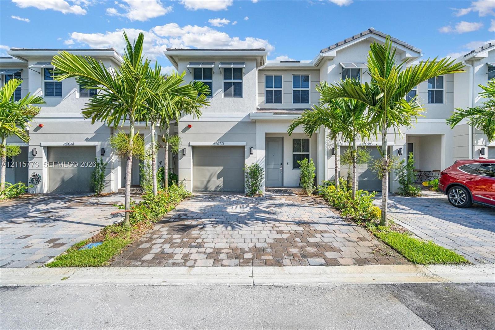 Multi-story residential exterior featuring stucco siding, paved driveway, attached garage, and metal-framed window awnings