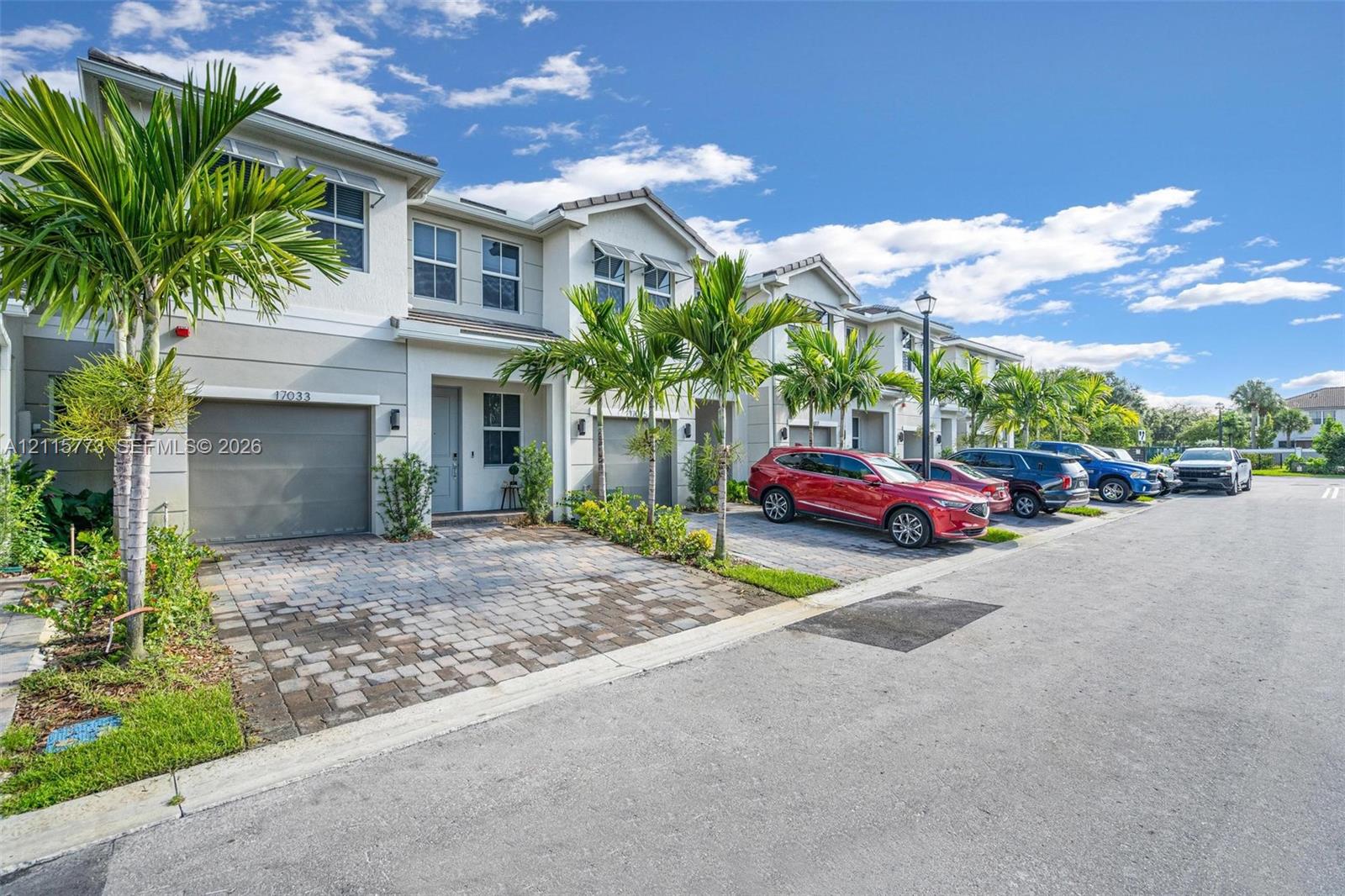 Multi-story townhome exterior featuring a stucco facade, paver driveway, attached garage, and metal window awnings Multi-story townhome exterior featuring a stucco facade, paver driveway, attached garage, and metal window awnings