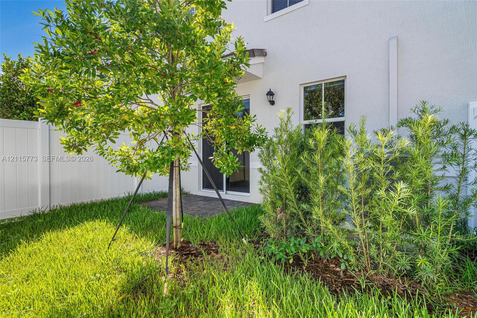 Private outdoor space featuring a paved patio, white vinyl privacy fencing, landscaped garden beds, and manicured lawn