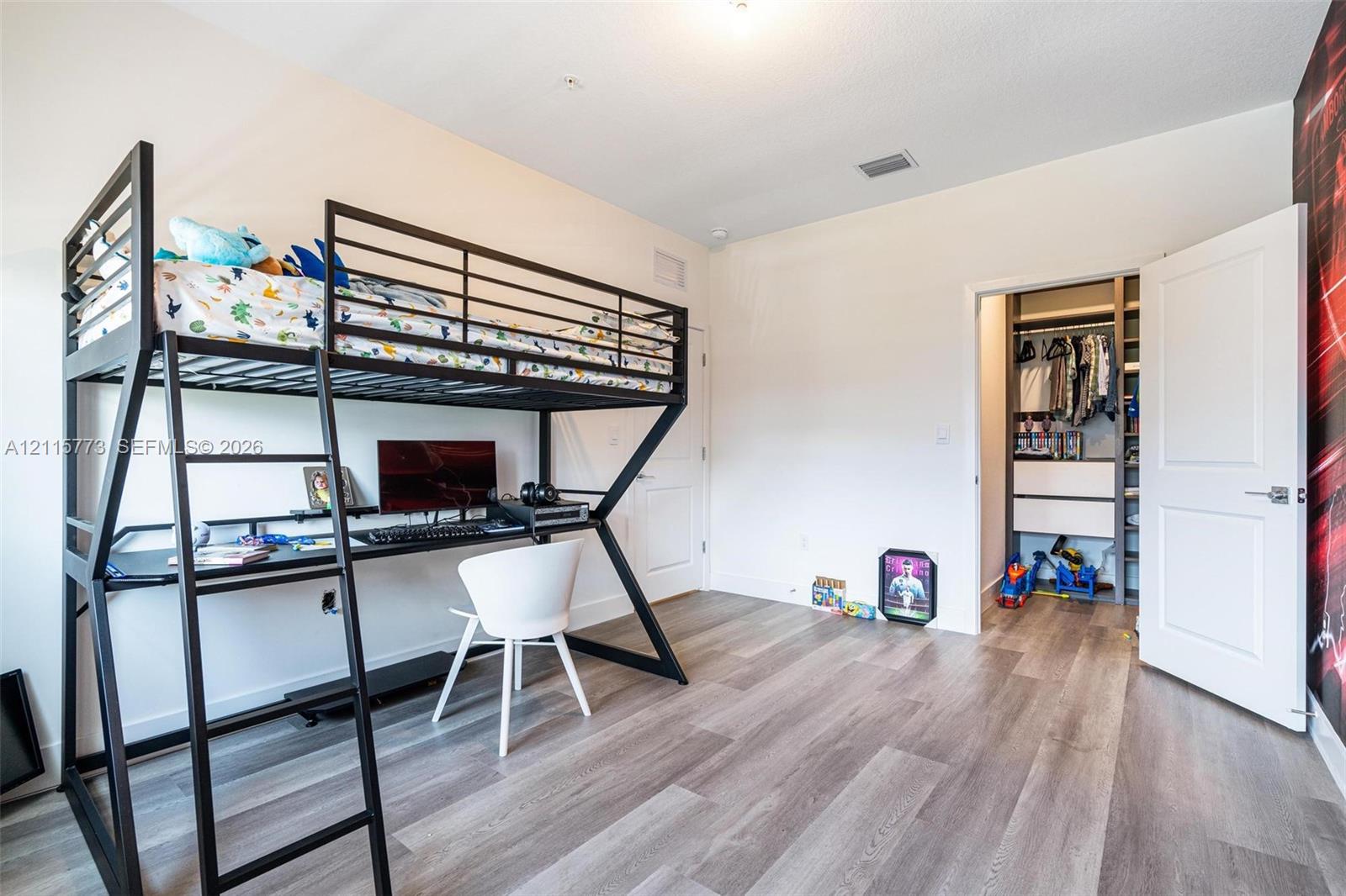 Interior space featuring light-toned wood-finish flooring, high ceilings, and a walk-in closet equipped with built-in shelving and drawers