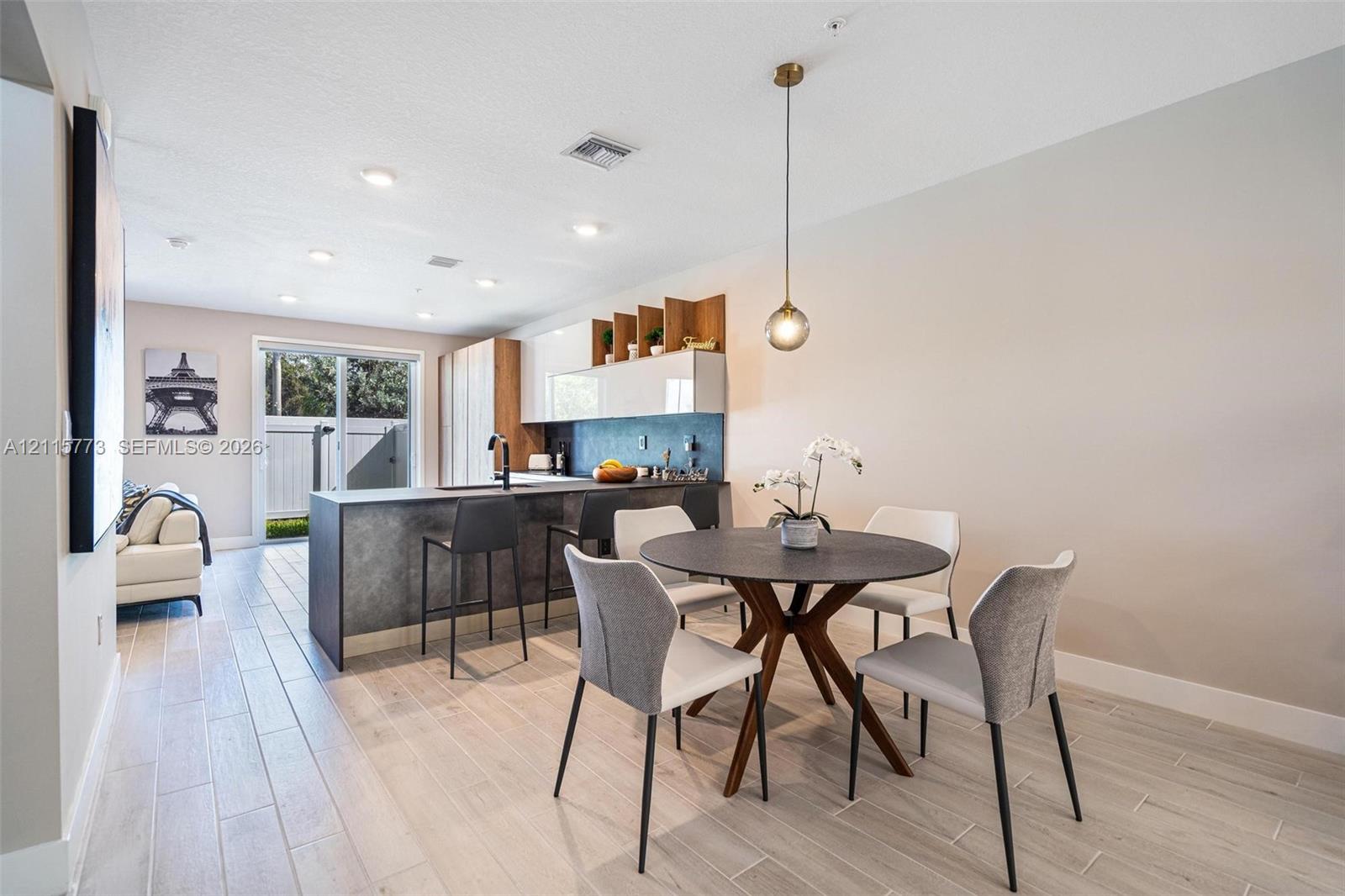 Kitchen featuring a textured charcoal island, wood-finish cabinetry with glossy white upper cupboards, recessed lighting, and wood-finish flooring Kitchen featuring a textured charcoal island, wood-finish cabinetry with glossy white upper cupboards, recessed lighting, and wood-finish flooring