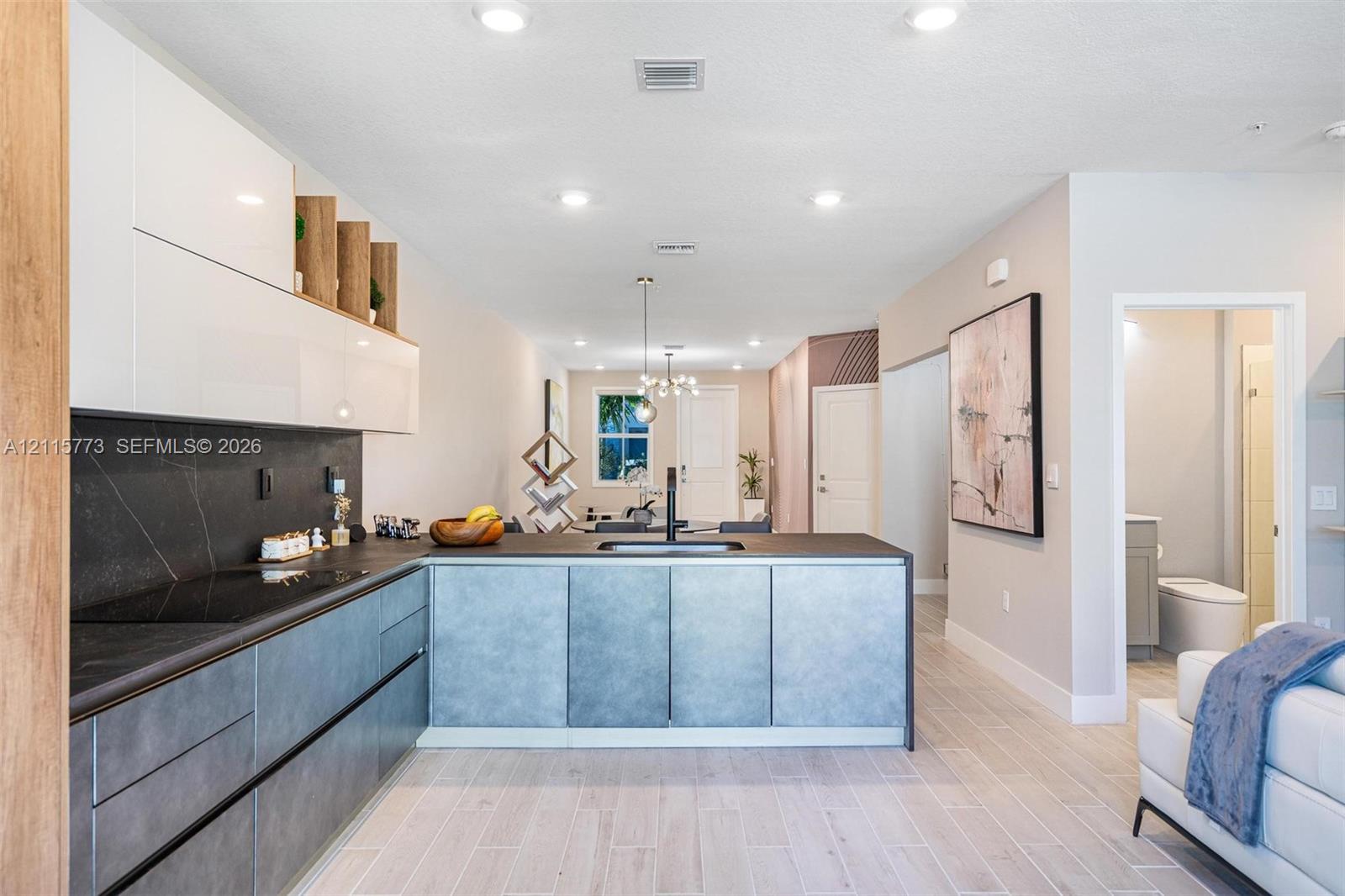 Contemporary kitchen featuring white high-gloss upper cabinetry, dark stone-finish countertops, grey lower cabinetry, integrated black hardware, and wood-finish flooring Contemporary kitchen featuring white high-gloss upper cabinetry, dark stone-finish countertops, grey lower cabinetry, integrated black hardware, and wood-finish flooring